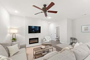 A living room with a grey couch, a fireplace, and a television mounted on the wall.