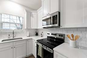 A white kitchen with a black stove and a black microwave.