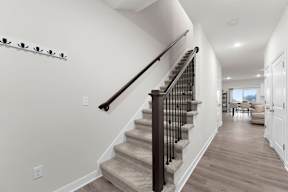 A staircase with a black railing and beige carpeted steps leads to a living room.