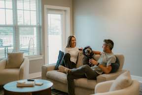 A man and woman sitting on a couch with a dog between them.