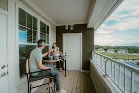 A man and woman are sitting at a table on a balcony.