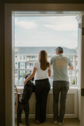 A man and woman standing by a window with a dog.