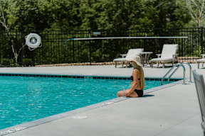A woman in a black bikini sits by a pool.