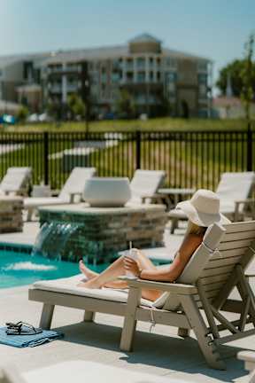 A woman in a white hat is lounging on a sunbed by a pool.
