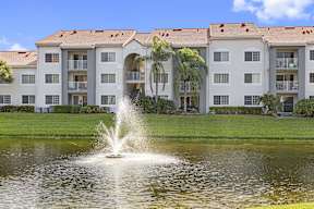 a fountain in the middle of a pond in front of some buildings