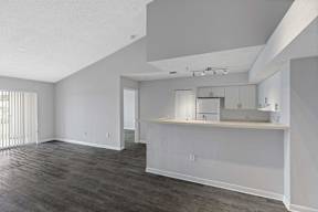 the living room and kitchen of an apartment with white walls and wood floors