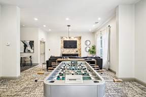 A foosball table is in the middle of a room with a couch and a television.