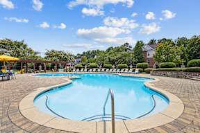 A large outdoor swimming pool surrounded by a stone patio and lounge chairs.