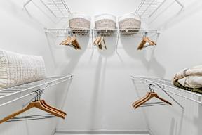A white closet with clothes hanging on hangers.