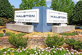 A sign for Halston South Point is displayed in front of a brick wall and greenery.