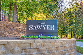 A sign that says "The Sawyer" is in front of a brick wall and trees.