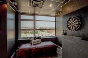 A dartboard hangs on a wall next to a window with a view of a cityscape.
