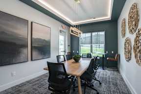 A conference room with a long table and chairs, a painting on the wall, and a view of the outdoors through a window.