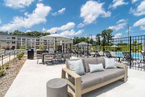A sunny day at the poolside with a sofa and chairs.