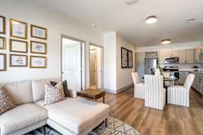 A living room with a white couch and a kitchen in the background.