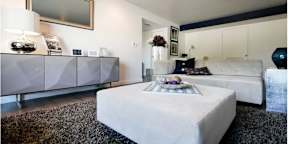 A white ottoman sits in the middle of a room with a grey rug.