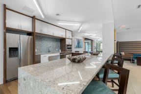 a kitchen with a large island with granite counter tops and a stainless steel refrigerator