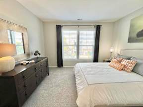 A bedroom with a large bed, a dresser, and a window with black curtains.