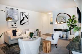 A living room with a grey couch, white chairs, and a black and white artwork on the wall.