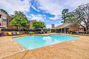 A pool surrounded by chairs and trees with a building in the background.