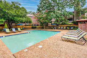 A pool surrounded by trees and chairs.