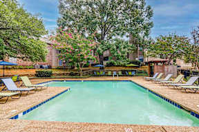 A pool surrounded by trees and chairs.