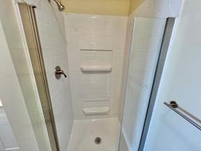 A white tiled shower with a drain in the middle.