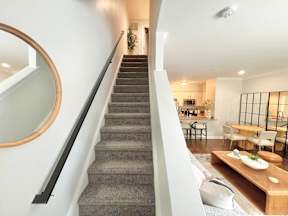 A staircase with a grey carpeted runner leads up to a brightly lit living room.