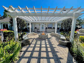A white pergola is over a patio with a fire pit.