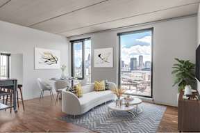 A living room with a white couch, a coffee table, and a large window with a view of the city.