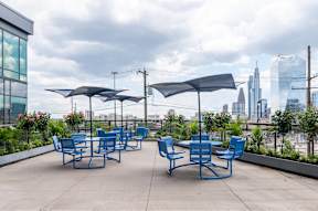 A patio with blue chairs and umbrellas overlooking a city skyline.
