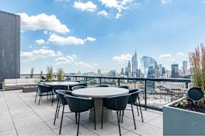 A table with chairs is set up on a rooftop terrace with a city skyline in the background