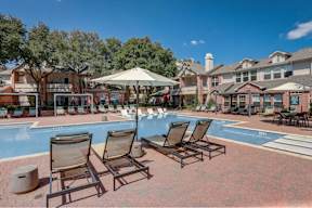 a pool with chairs and umbrellas in front of apartment buildings