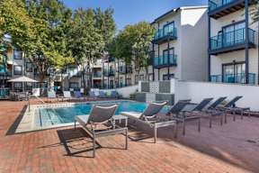 an outdoor pool with lounge chairs in front of an apartment building