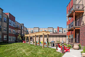A sunny day at a modern apartment complex with a grassy area and a wooden pergola.