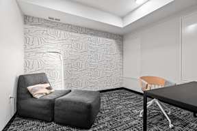 A grey couch with a pillow sits in front of a wallpapered wall.