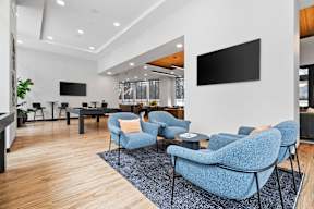 A modern living room with blue chairs and a flat screen TV mounted on the wall.