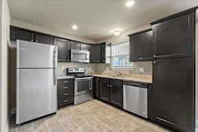 Peculiar, MO, Townhomes Near Raymore-Peculiar School District - Bradley’s Crossing - Kitchen with Vinyl Plank Flooring, Granite Countertop, Custom Cabinetry, and Stainless Steel Appliances.
