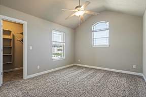 A room with a ceiling fan and two windows.