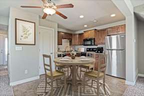 Townhomes for Rent in Peculiar, MO - Bradley’s Crossing - Dining Room with High Ceiling, Ceiling Fan with Light, Vinyl Plank Flooring, 4-Seater Dining Table and Chairs, Round Rug, and Wall Art.