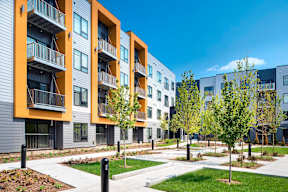 A modern apartment complex with balconies and trees in the foreground.