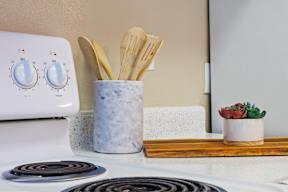 A white stove top with a pot of wooden utensils on it.