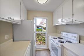 Santa Clara, CA, Affordable Apartments Near Levi's Stadium - Montecito Apartment Homes - Kitchen with Wood-Style Flooring, White Cabinetry, White Appliances, Ceiling Light, and Large Window.
