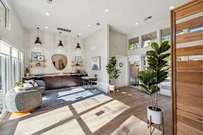 A modern living room with a large window, a grey sofa, a wooden floor, and a potted plant.