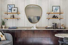 A modern kitchen with a grey chair and a round mirror above a counter.
