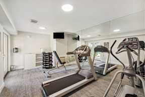 Santa Clara, CA, Pet-Friendly Affordable Apartments - Montecito Apartment Homes - Fitness Center with Treadmills, Weight Bench, Dumbbells, Mounted TV, Shelves, Floor-To-Ceiling Mirrors, and Lighting.
