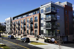 A row of modern apartment buildings with cars parked in front.