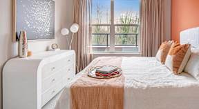 A bedroom with a white bed, a white dresser, and a window with a view of trees.