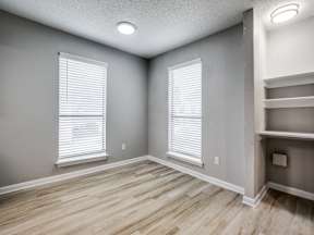 A room with wooden floors and two windows with blinds.