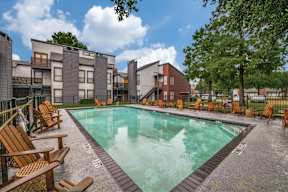 A swimming pool surrounded by wooden chairs and buildings.